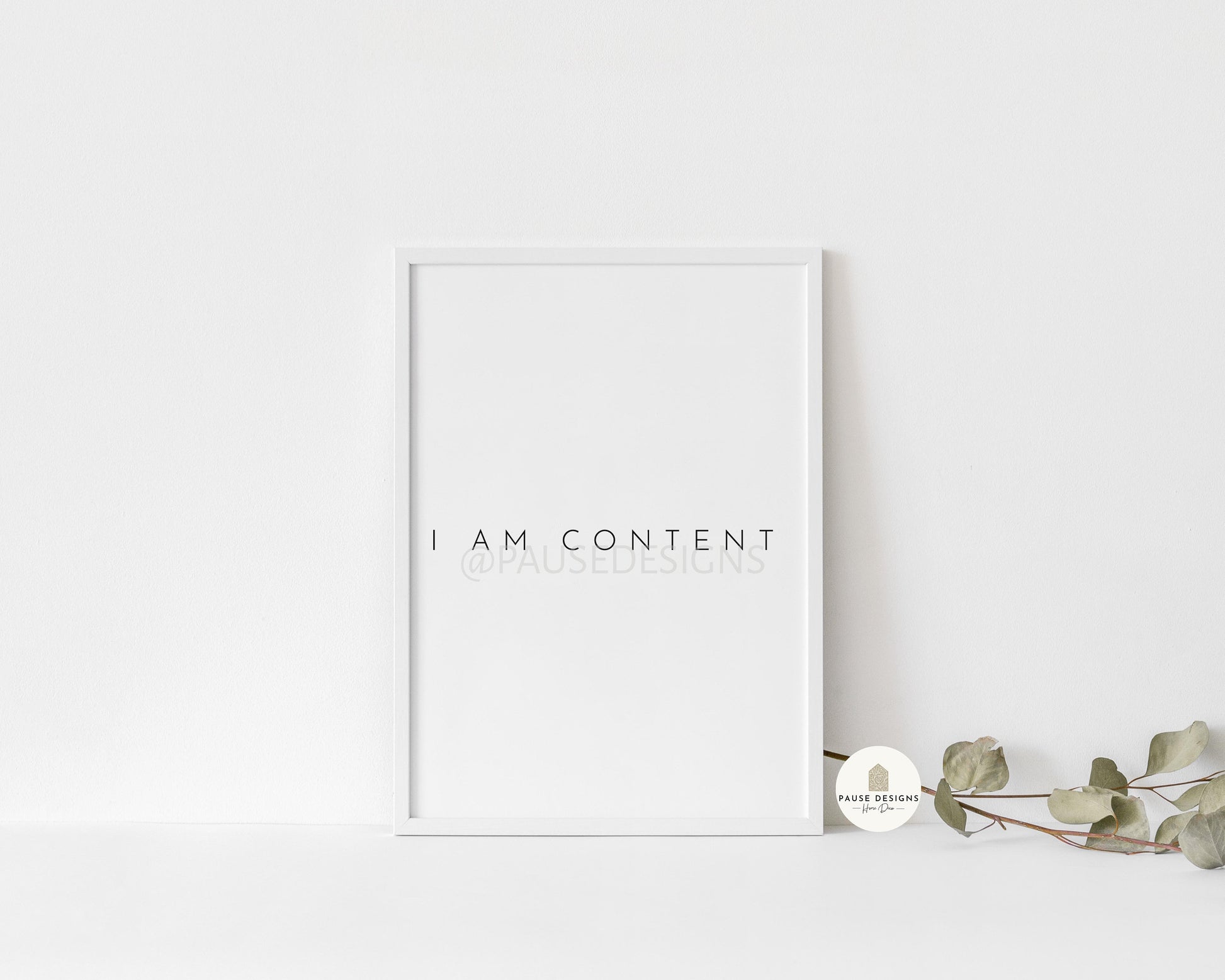 a white picture frame sitting on top of a table next to a plant